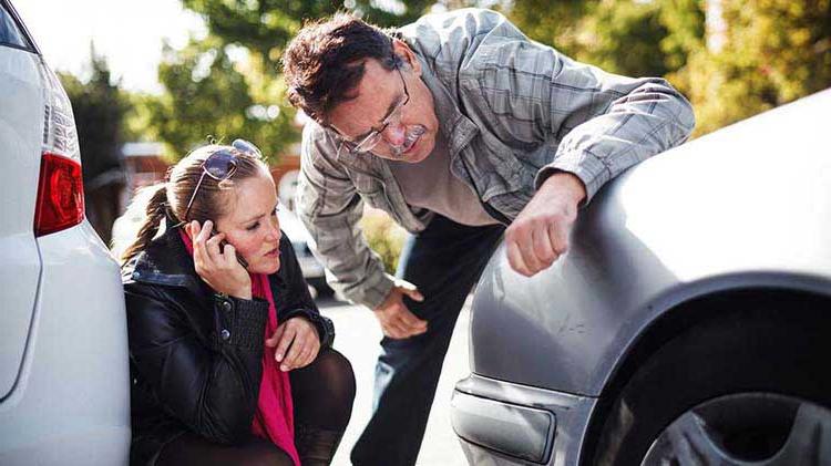 Two people looking at dents on a car in a parking lot.